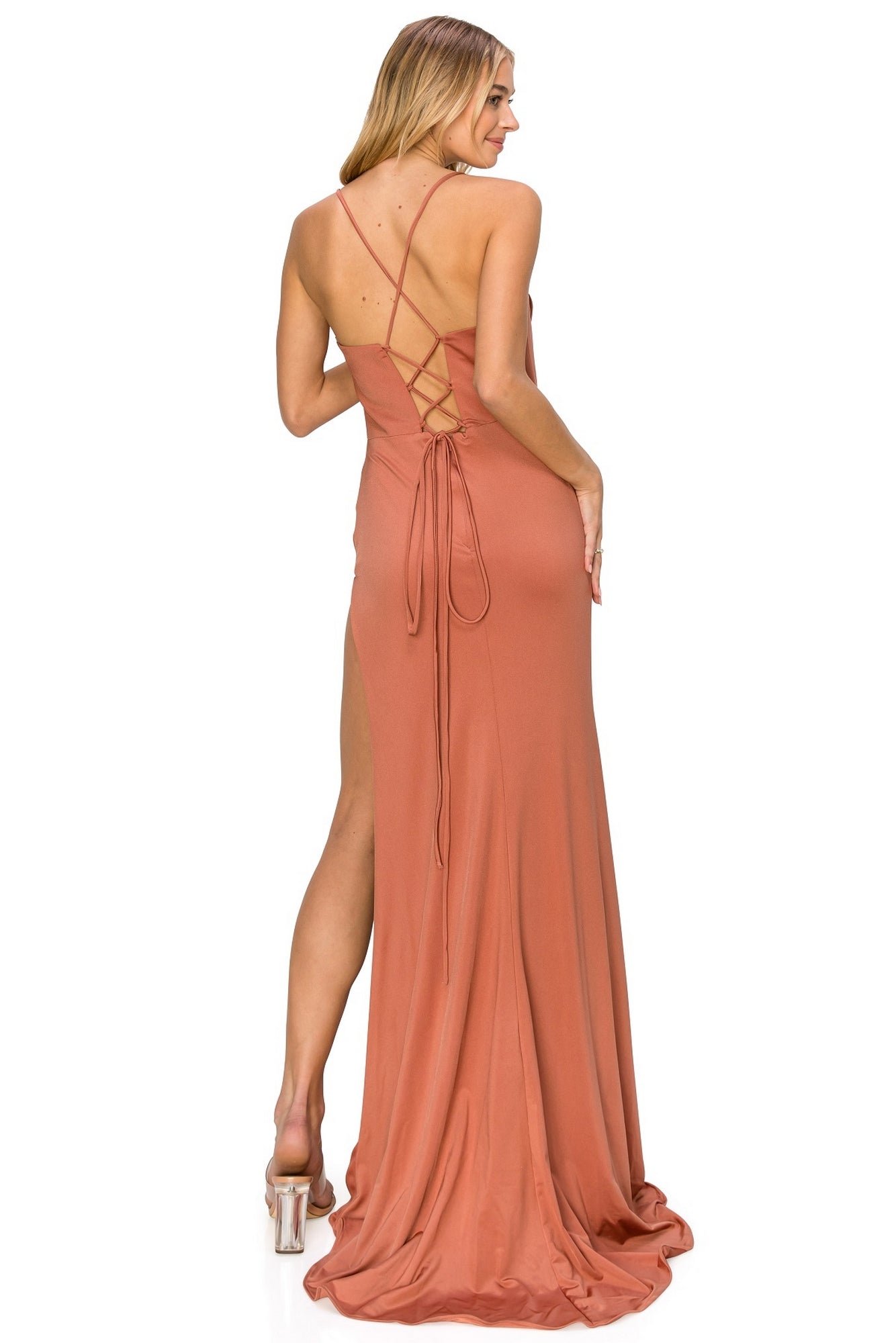 A woman wears the Cowl-Neck Long Formal Corset Prom Dress 8035J, a floor-length rust gown with a cowl neck, lace-up open back, high slit, and clear high-heeled shoes.